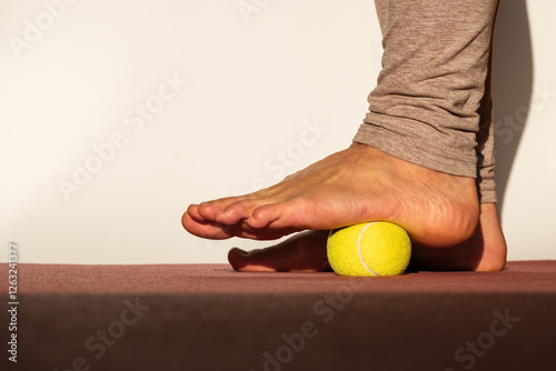 Myofascial relaxation of the muscles of the foot with a tennis ball on a mat at home, close-up. Concept on the topic of preventing foot pain
