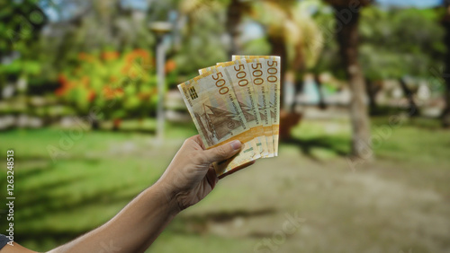 Man holding norwegian krone banknotes in an outdoor park setting, with greenery in the background, reflecting an informal financial transaction or casual cash exchange scenario. photo