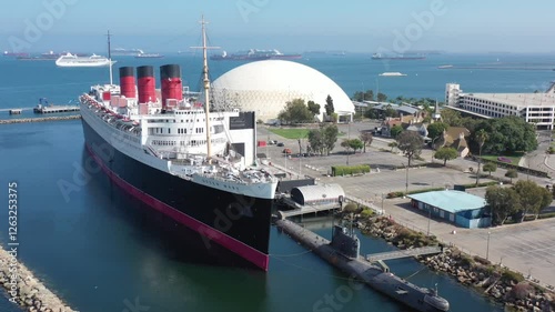 Aerial Drone Footage of the Historic Queen Mary Cruise Ship Docked at Long Beach Harbor, California, Showcasing Maritime History and Coastal Leisure with Clear Blue Waters and a Bustling Harbor Scene