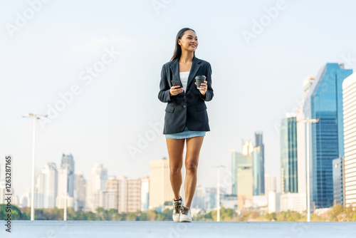 Foto Young Asian Businesswoman Holding Phone and Coffee Walking in Modern City Outdoo