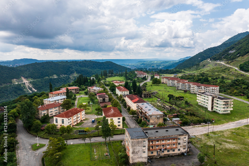 Obraz premium Aerial view of an abandoned residential settlement in the mountains. Rows of empty apartment buildings contrast with the surrounding green landscape, creating a post-apocalyptic atmosphere.