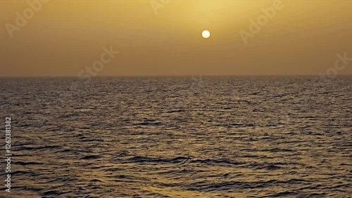 Sun low on the horizon through hazy amber clouds over peaceful ocean - View at sea