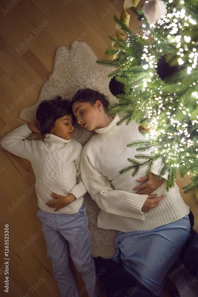 A mother in a white sweater with her son for 7 year on the floor by the Christmas tree in an apartment on New Year's Eve