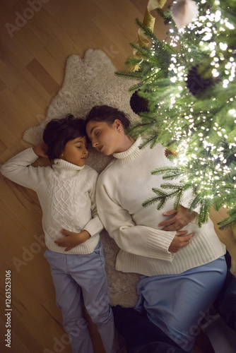 Obraz na płótnie A mother in a white sweater with her son for 7 year on the floor by the Christmas tree in an apartment on New Year's Eve w salonie
