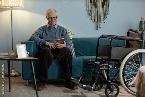 Canvas Print Full length shot of tech savvy grandfather using wheelchair sitting on sofa typi
