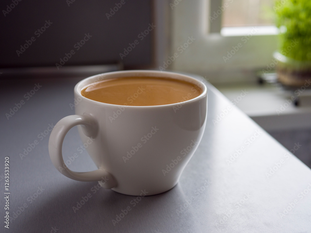 Large white mug full of coffee sitting on a table by a window with a small plant in a pot on the windowsill, enjoying a quiet moment with a warm beverage Large white mug full of coffee sitting on a table by a window with a small plant in a pot on the windowsill, enjoying a quiet moment with a warm beverage