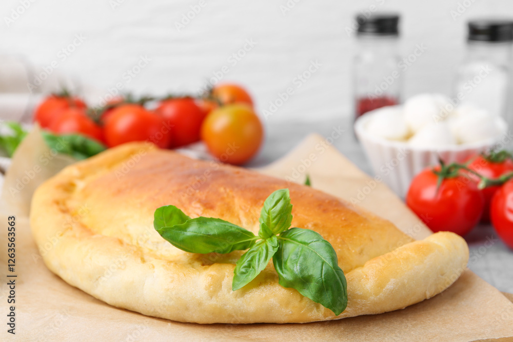 Tasty vegetarian calzone with basil and tomatoes on table, closeup