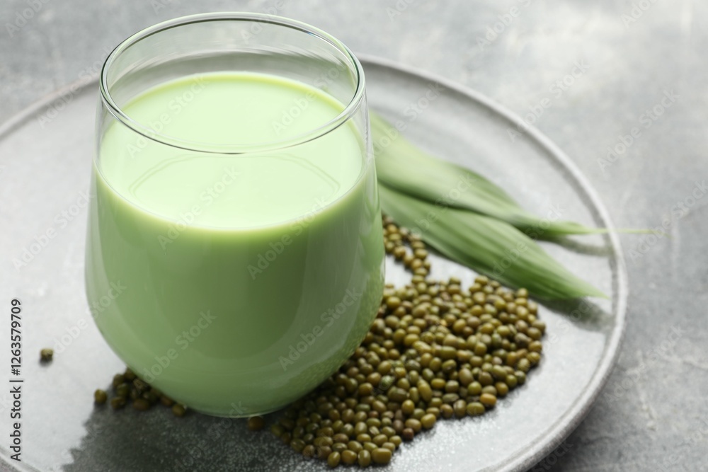 Fresh mung bean juice in glass, seeds and green leaves on grey table, closeup Fresh mung bean juice in glass, seeds and green leaves on grey table, closeup