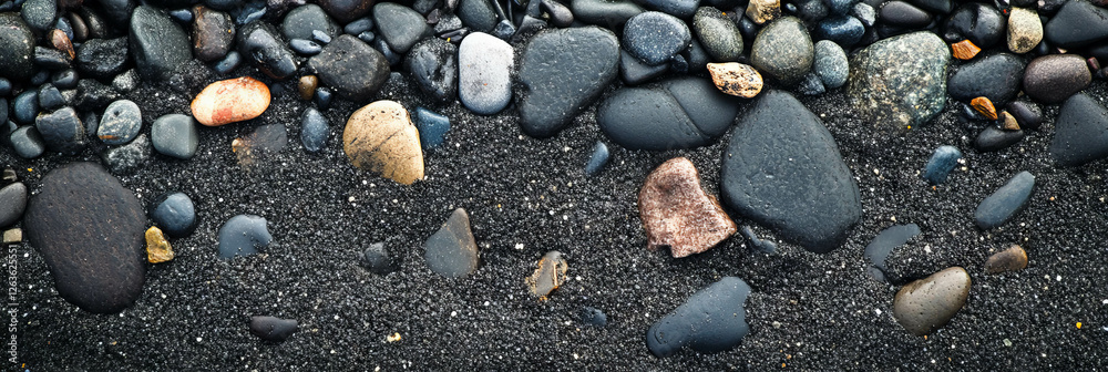 Black sand beach texture showcasing smooth pebbles in varied sizes under deep shadows Black sand beach texture showcasing smooth pebbles in varied sizes under deep shadows