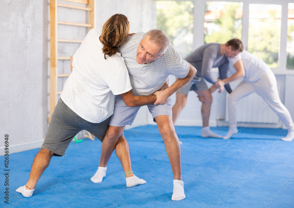Fototapeta premium Old man with sparring partner in gym during self-defense training, sparring and practicing technique of hip flip