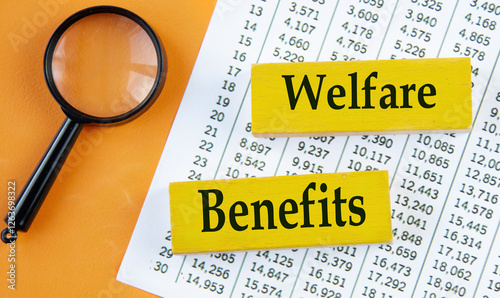 WELFARE BENEFITS - words on yellow wooden blocks on the background of a magnifying glass and a table with numbers
