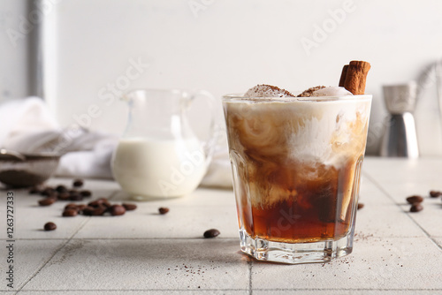 Glass of White Russian cocktail with cinnamon and coffee beans on white tile table photo