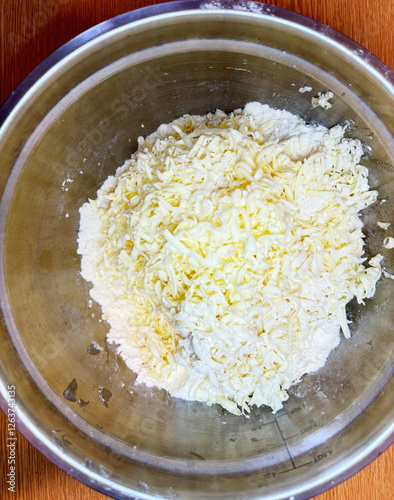 Grated cheese and flour mixture in a stainless steel bowl on wooden surface, ready for baking or cooking preparation. High quality photo photo
