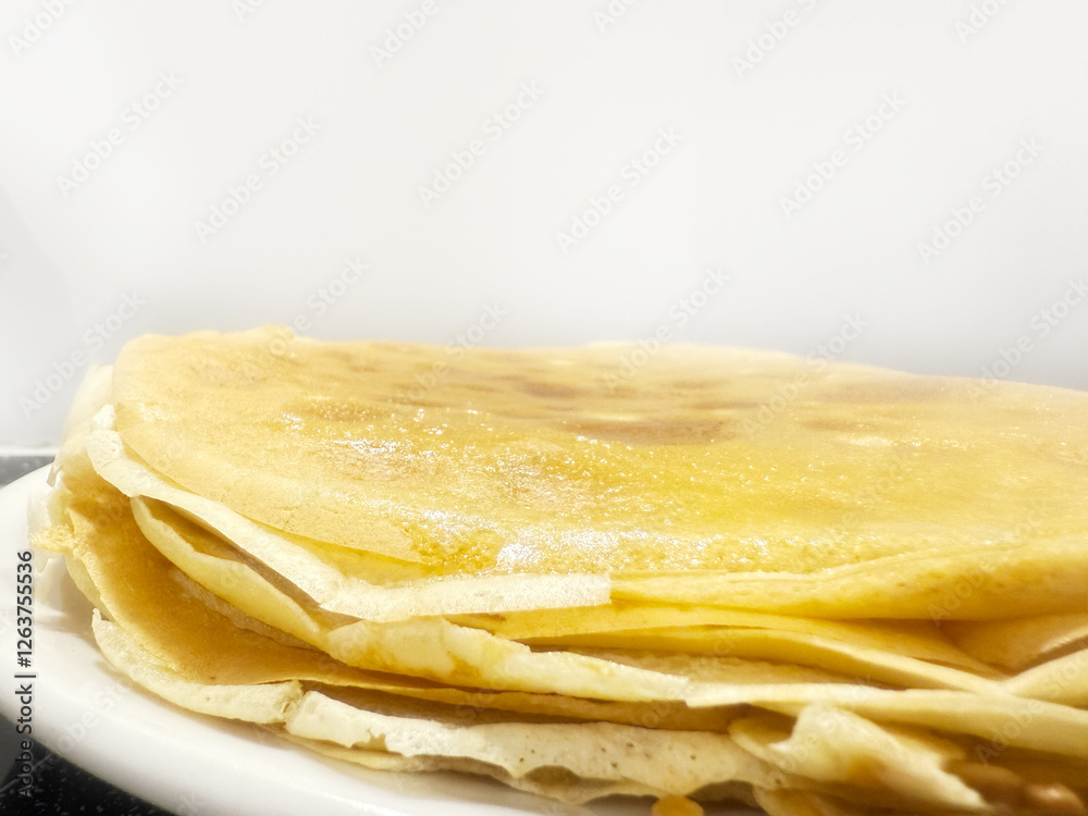 Stack of Thin Homemade Crepes with Golden Butter Glaze. High quality photo A delicious stack of thin, golden crepes with a buttery glaze, freshly made and served on a white plate. These homemade Stack of Thin Homemade Crepes with Golden Butter Glaze. High quality photo A delicious stack of thin, golden crepes with a buttery glaze, freshly made and served on a white plate. These homemade