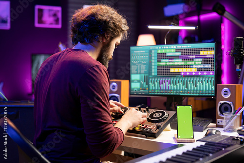 Foto Music engineer twisting pre amp knobs on mixing console in home studio, having phone with greenscreen layout