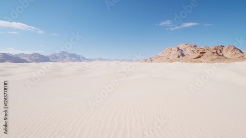 Vast white sand dunes stretch towards distant rocky mountains under a clear blue sky during a bright sunny day.