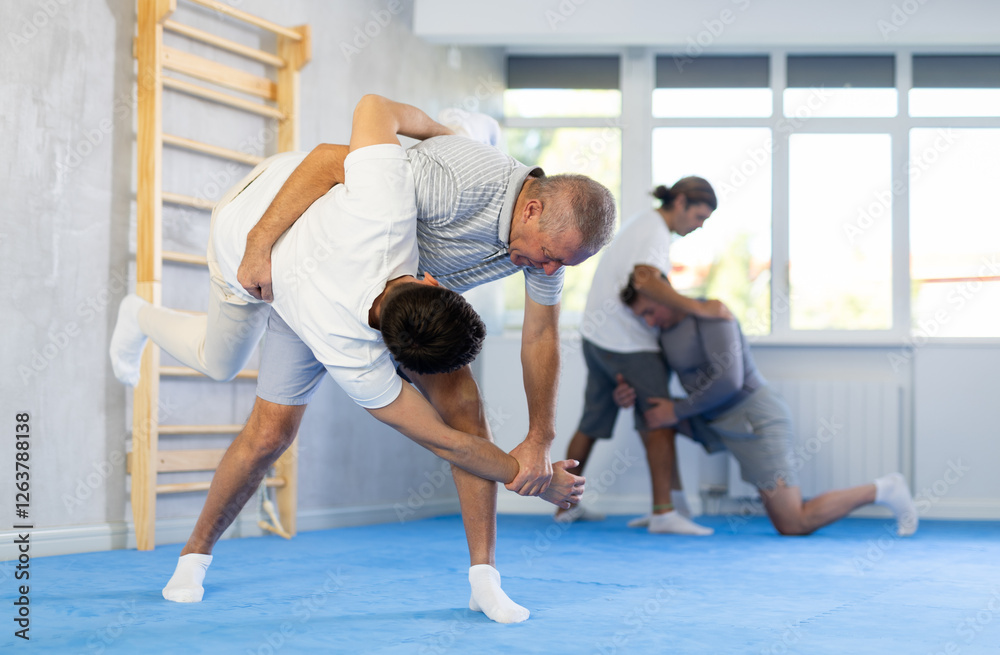 Two men of different ages in judo sparring - older man throws young guy to the mat Two men of different ages in judo sparring - older man throws young guy to the mat