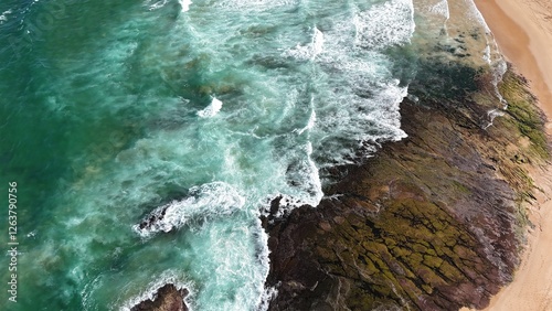 Drone shot aerial view of waves crashing onto rocks near a beach in summer in Australia 