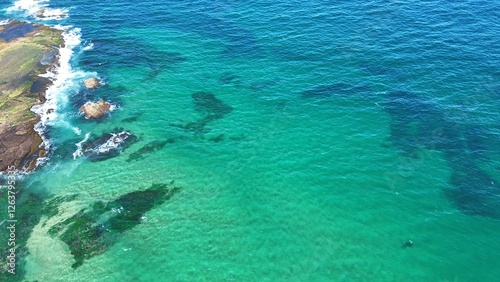 Drone shot aerial view of a reef with clear blue and turquoise water near a beach in Australia 