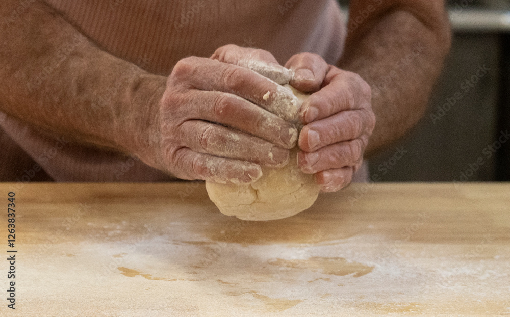 Closeup of an unrecognizable adult male holding a ball of pastry dough over a floured kitchen worktop. Closeup of an unrecognizable adult male holding a ball of pastry dough over a floured kitchen worktop.