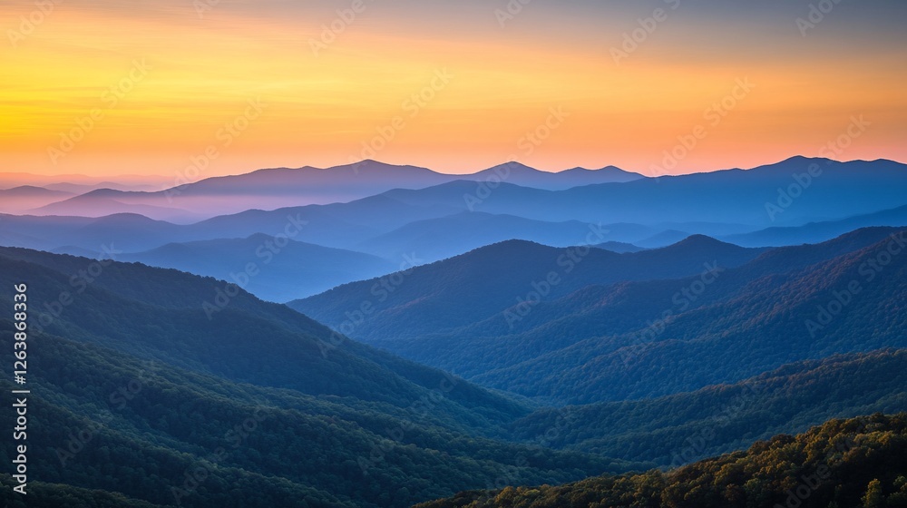 Fototapeta premium Serene sunset over layered blue mountains, hazy atmosphere.