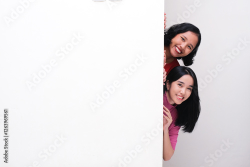 Two girls peeking behind a wall with happy face photo