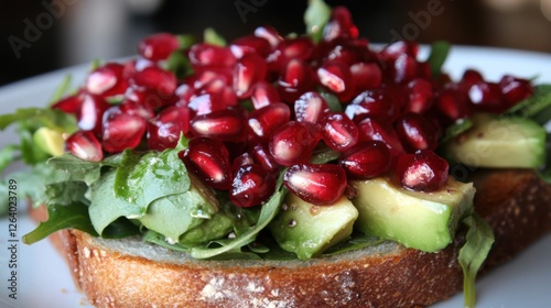 A healthy open-faced sandwich with avocado, greens, and pomegranate seeds on whole grain bread. photo