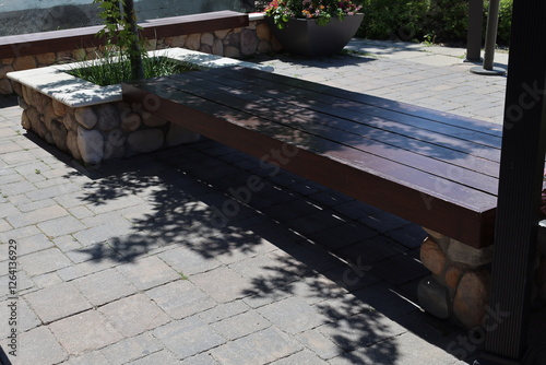 long wide shady wooden bench on landscaped patio on sunny summer day