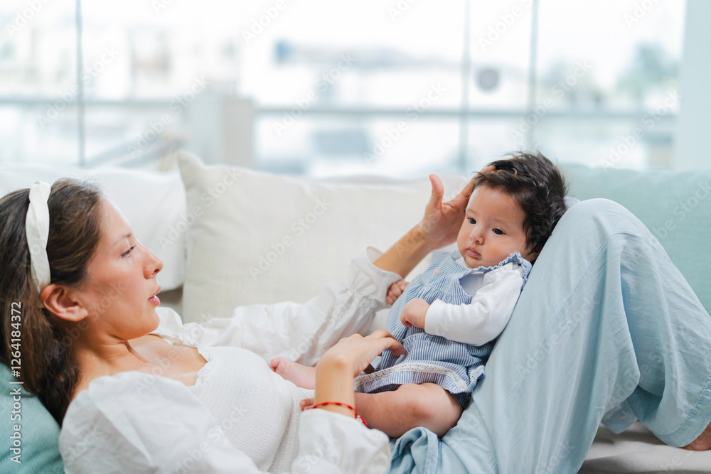 Obraz premium Mother lying on sofa playing and stimulating her baby girl