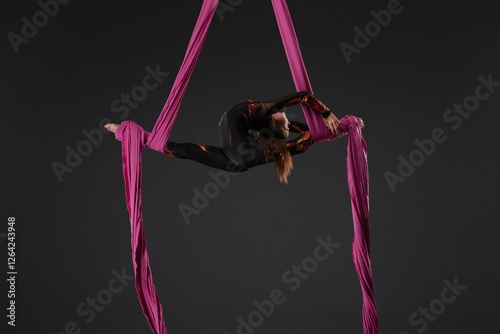 Girl performs aerial gymnastics using pink fabric suspended from a pole