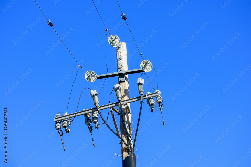 Electrical utility wooden pole with multiple insulators, wires and power lines against a vibrant blue sky Electrical utility wooden pole with multiple insulators, wires and power lines against a vibrant blue sky