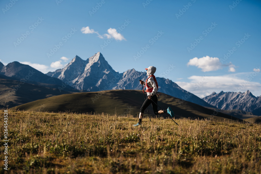 Fototapeta premium Woman trail runner running on grassland with rocky mountains in the distance