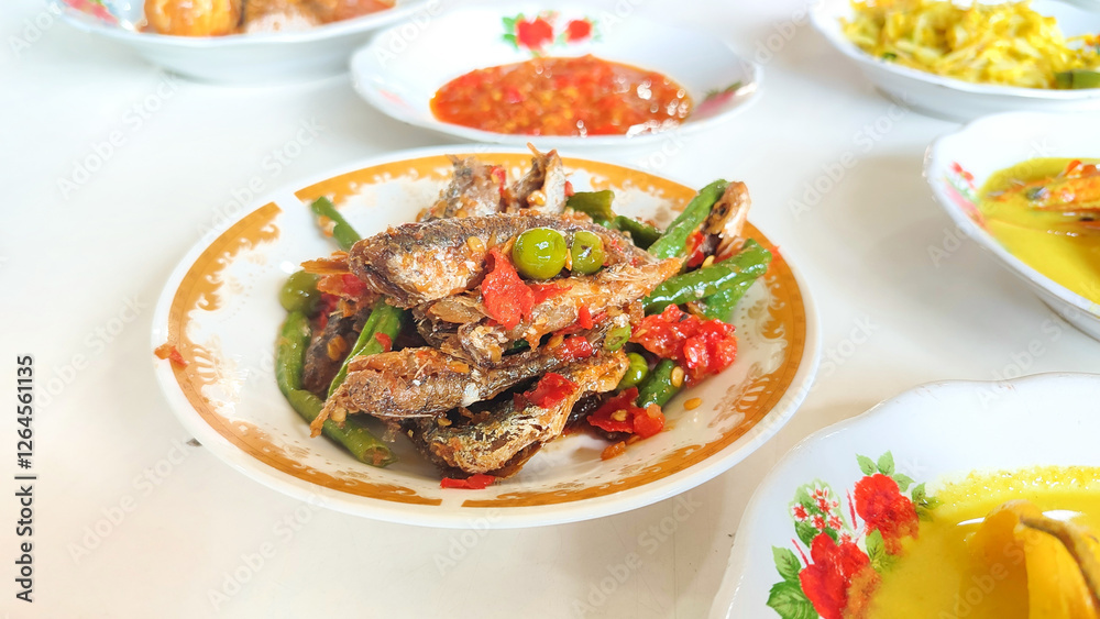 Various menus on white plates from a Padang cuisine restaurant consisting of fried small fish with red chilli arranged in neat pile table. Minang or Minangkabau food. Various menus on white plates from a Padang cuisine restaurant consisting of fried small fish with red chilli arranged in neat pile table. Minang or Minangkabau food.