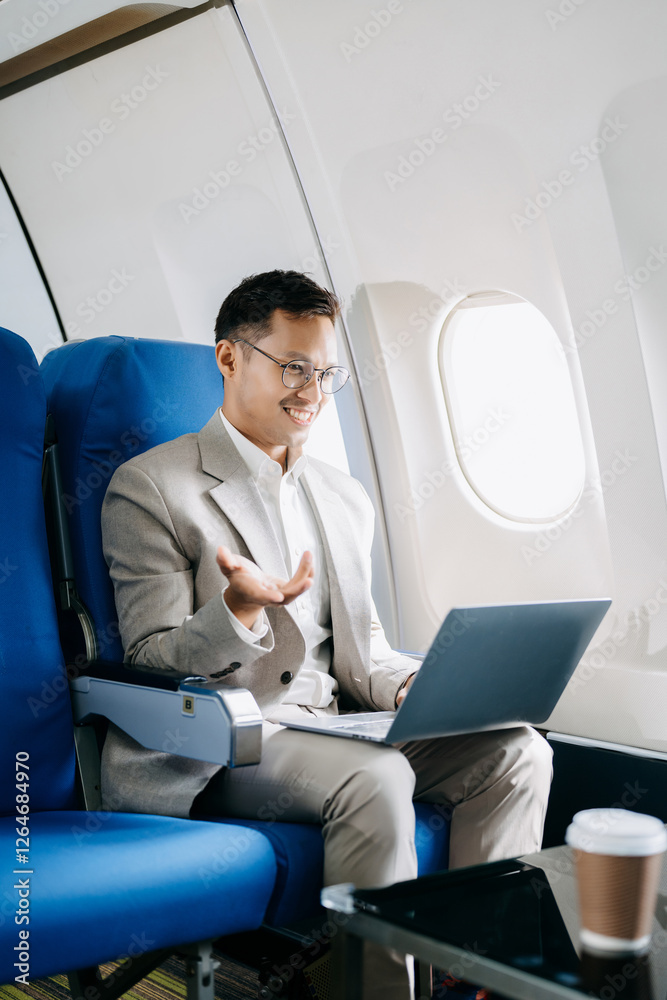 Fototapeta premium Attractive Asian male passenger of airplane sitting in comfortable seat while working laptop and tablet with mock up area using wireless connection.