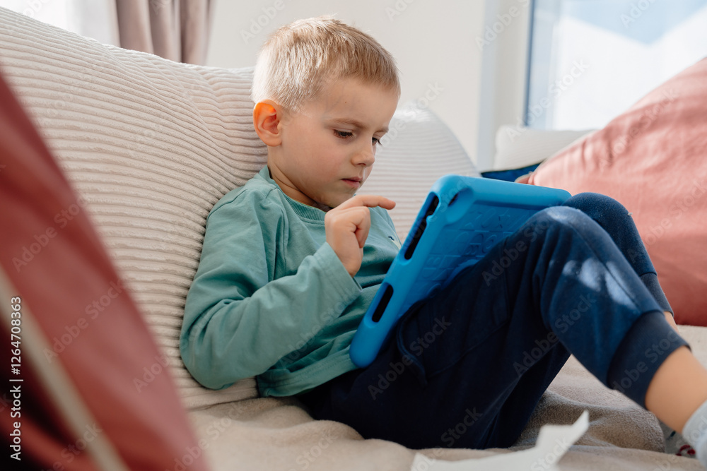 a 4-year-old boy sits on the sofa at home with a tablet. High quality photo a 4-year-old boy sits on the sofa at home with a tablet. High quality photo