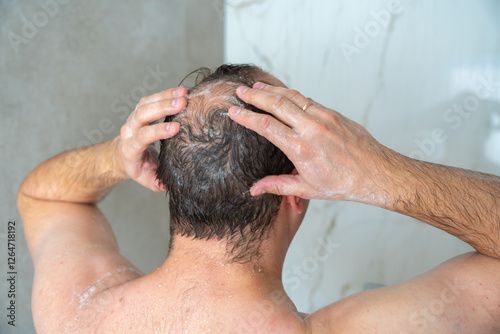 man soaps his head in the shower, head with a bald spot, standing with his back to the camera, close-up shot. High quality 4k footage
