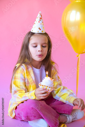 happy little girl celebrating her birthday, blowing candle on cake on pink background