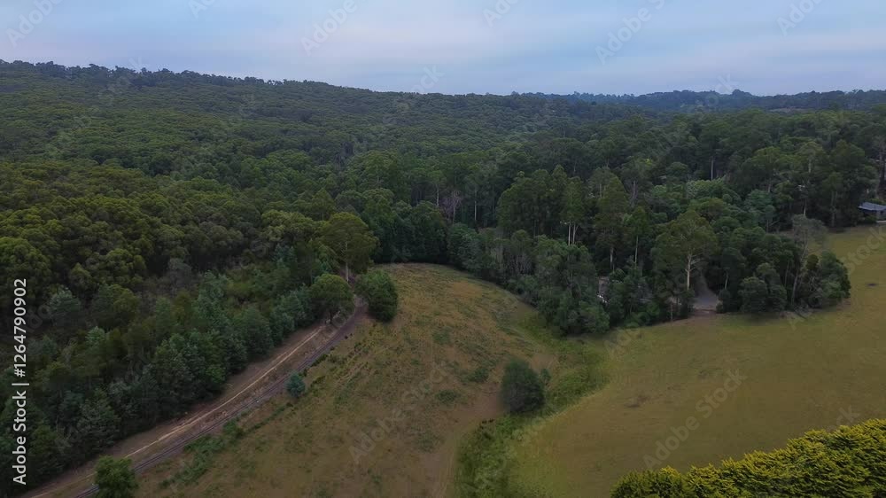 Aerial shot moving backwards showing a railway line running through bushland and rural farms in Australia. Aerial shot moving backwards showing a railway line running through bushland and rural farms in Australia.