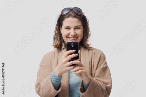 Happy woman looking at camera and holding her smartphone