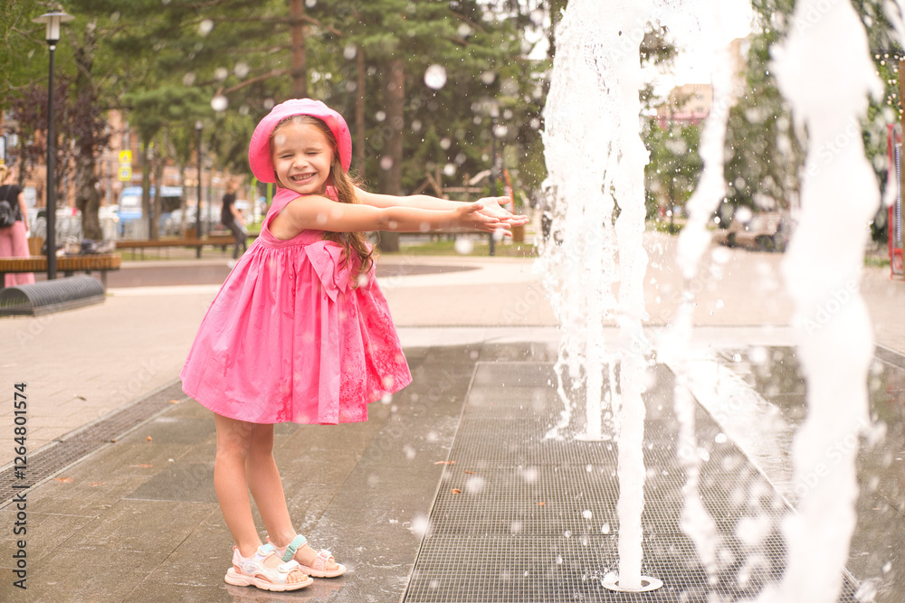 Naklejka premium kid girl in pink dress plays next to fountain on summer day