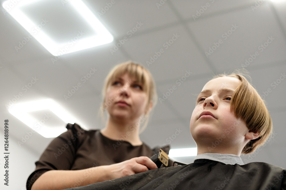 Fototapeta premium Child receiving haircut from stylist in modern barber shop during daytime