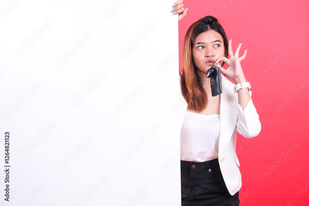 A woman with long hair holds car keys near her mouth while standing next to a white board, isolated on a red background