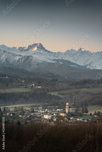 The peaks of Palas and Balaitous dominate the horizon above the village of Montgaillard, creating a striking contrast between the snow-covered summits and the rural landscape below photo