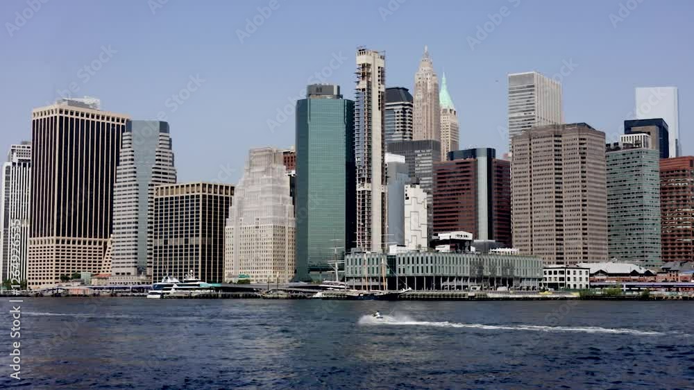 A captivating view of the Manhattan skyline from the East River, featuring towering skyscrapers, a mix of modern and historic architecture, and a jet ski speeding across the water, adding a sense of m A captivating view of the Manhattan skyline from the East River, featuring towering skyscrapers, a mix of modern and historic architecture, and a jet ski speeding across the water, adding a sense of m