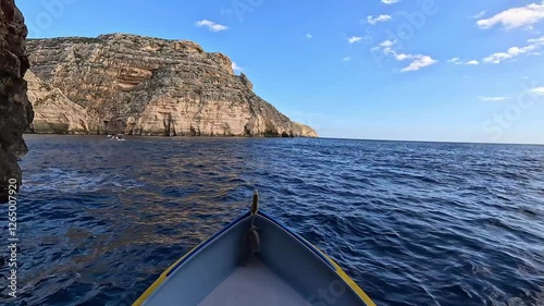 A boat approaches the Blue Grotto in Malta, surrounded by limestone cliffs and deep blue waters. A popular tourist destination known for its sea caves and crystal-clear reflections.