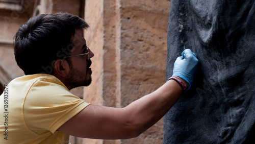 close-up of young caucasian male art restorer using scalpel on bronze statue with latex gloves