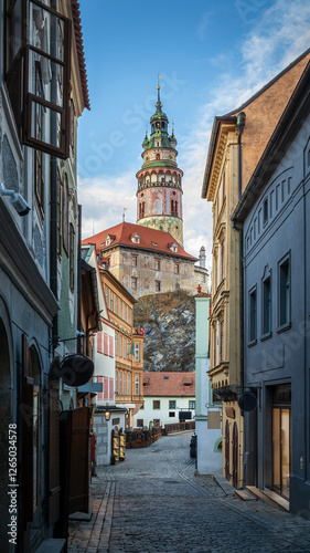 A charming cobblestone street in Сesky Krumlov, Czech Republic, at sunrise. The historic tower rises above colorful medieval buildings, bathed in soft morning light, creating a picturesque scene.