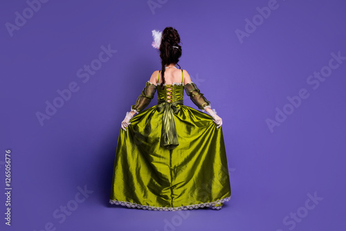 Elegant woman in green period costume with lace holding skirt against violet background
