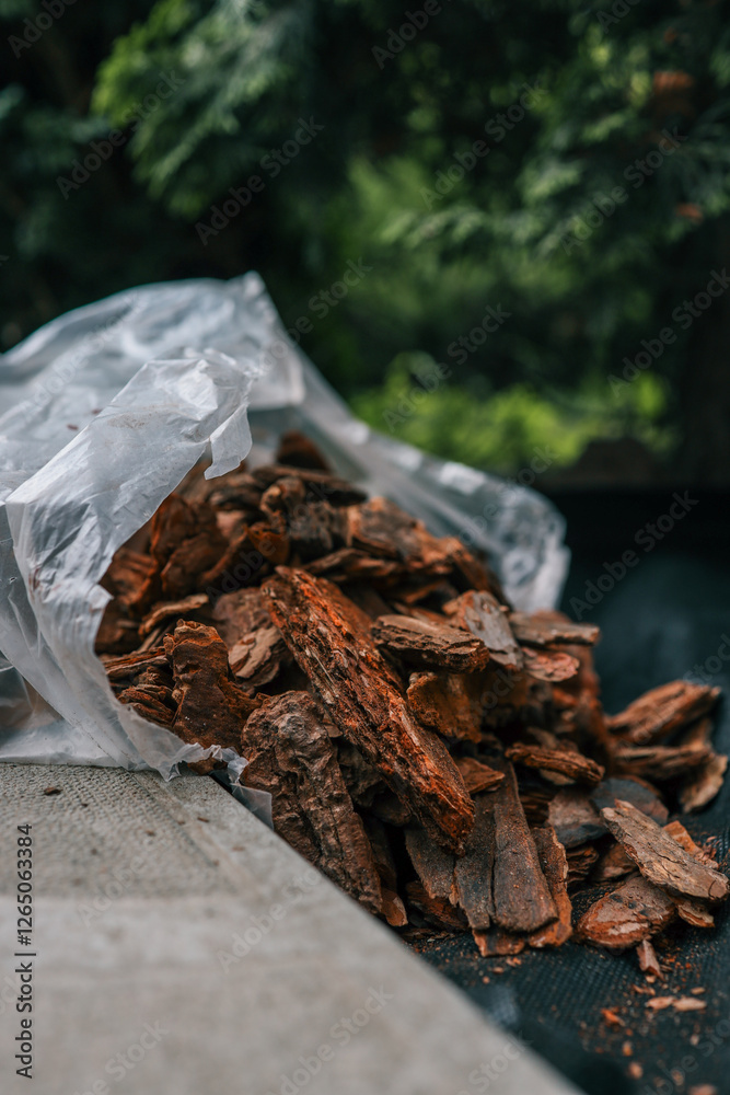 Bag of decorative bark mulch on black landscaping fabric near paving stones and green bushes. Used for soil protection, moisture retention, and weed control in garden landscaping Bag of decorative bark mulch on black landscaping fabric near paving stones and green bushes. Used for soil protection, moisture retention, and weed control in garden landscaping