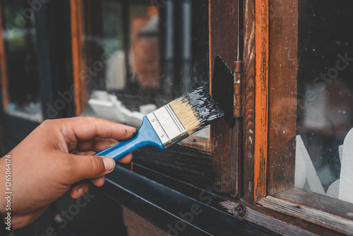 Close-up of a hand painting a wooden window frame black with a brush. Home improvement project for renovation, restoration, or maintenance of an old wooden surface photo